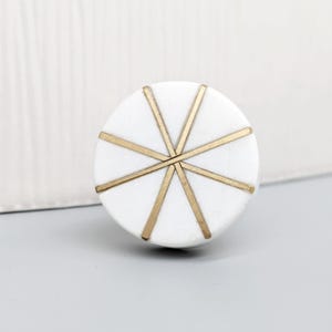May include: White round cabinet knob with a gold starburst design.
