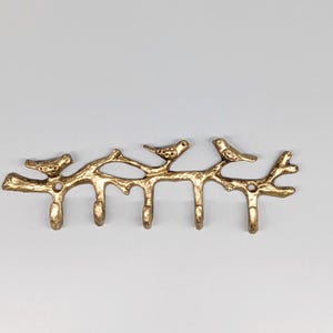 May include: A gold-coloured metal wall hook featuring a branch design with three small birds perched on it. The branch has four hooks for hanging items. The decorative piece is designed to be mounted on a wall.