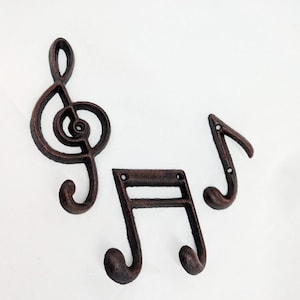 以下が含まれることがあります： 音楽の記号の形をした鋳鉄製のフックが3つ。フックはさびた茶色です。フックは、鍵、タオル、その他の物を掛けるのに最適です。