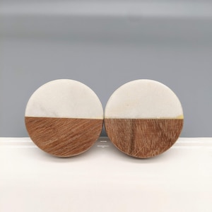 Op de afbeelding: Twee ronde houten en witte marmeren ladegrepen. Elke greep is half wit marmer en half bruin hout.