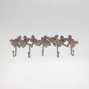 Puede incluir: Un perchero de pared decorativo de metal con seis diseños de libélulas. Los ganchos son curvos y las alas de las libélulas están detalladas. Ideal para colgar objetos.