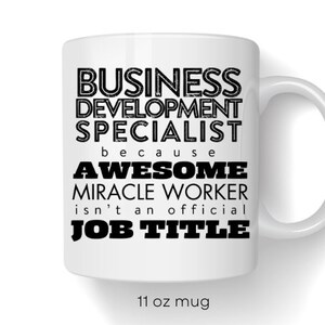 May include: White ceramic mug with black text that reads "BUSINESS DEVELOPMENT SPECIALIST because AWESOME MIRACLE WORKER isn't an official JOB TITLE". The mug is 11 ounces.