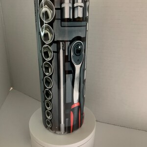 May include: A stainless steel tumbler with a black, white, and red design featuring a variety of tools, including wrenches, sockets, and screwdrivers.