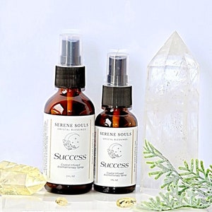 May include: Two brown glass bottles with black spray tops and white labels. The labels read "Serene Souls Crystal Blessings Success Crystal Infused Aromatherapy Spray" with a crescent moon and star design. The larger bottle is 2 fl oz and the smaller bottle is 1 fl oz.