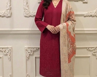 May include: A burgundy-colored, long-sleeved outfit with matching pants. The top features intricate embroidery and a V-neck. A patterned shawl in beige and orange is draped over the shoulders. The outfit is suitable for formal occasions.