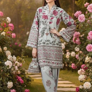 May include: A light blue floral print outfit, including a long-sleeved tunic and matching pants. The tunic features a mandarin collar and a floral pattern in shades of pink and green. A small matching handbag is held in the hand.