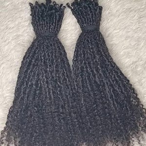 Może przedstawiać: Dwa pakiety czarnych przedłużaczy włosów ludzkich w kręconym stylu dredów. Włosy są długie i grube, a końcówki są lekko strzępione.