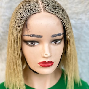 May include: A blonde wig with small braids, styled in a bob. The wig is made with a lace front and is worn on a mannequin head.