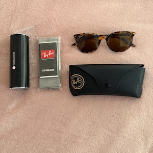 May include: Sunglasses and accessories set. Includes tortoiseshell sunglasses, a black leather case, a microfiber cleaning cloth, and a black cylindrical case with the text "sunglass hut".