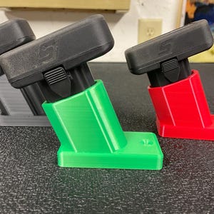 May include: Three angled black and colored plastic mounts. One is gray, one is green, and one is red. Each has a black top with a logo and a lever. The mounts are on a dark surface.