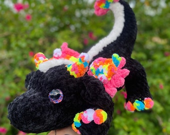 May include: A black crocheted dragon with colorful, pink, yellow, and blue accents. The dragon has a long tail and large, sparkling eyes.