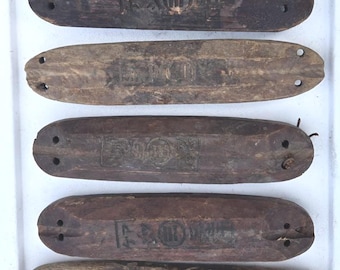 May include: Five elongated, rectangular wooden blocks with rounded ends, each featuring two small holes at both extremities. The dark, weathered wood surfaces display stamped Japanese characters and circular symbols centred on each piece.