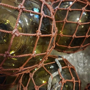Op de afbeelding: Close-up van verschillende ronde glazen boeien bedekt met een bruin net. De boeien zijn lichtgroen en het net is donkerbruin.