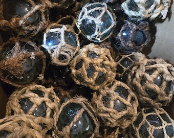 May include: A collection of glass fishing floats wrapped in natural twine. The floats are various shades of blue and green, and some have a net-like pattern.