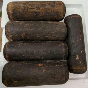 May include: Five cylindrical wooden blocks with a dark, weathered finish and visible grain. Each block features carved Japanese characters on its surface. The wood shows signs of wear, including small chips and variations in the dark brown colour.