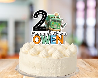 May include: A white cake with white frosting and a green and yellow cake topper that says "Happy Birthday Owen" and features a cartoon truck with a number 2 on the side.