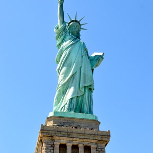 May include: A green statue of the Statue of Liberty on Liberty Island in New York City. The statue is standing on a stone pedestal with a torch held high in her right hand.