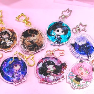 May include: A set of ten colourful anime character keychains. Each keychain features a different character with unique details and a clear background. The keychains are attached to gold-coloured chains with various charms.
