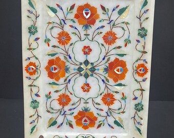 Könnte beinhalten: Ein weißes Marmortablett mit einem floralen Design, das mit bunten Steinen eingelegt ist. Das Tablett steht auf einem Holzständer.