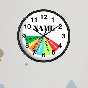 May include: A round wall clock with a black frame and a white face. The clock face is segmented into colourful sections, each labelled with an activity, such as "Homework" and "Play Time". The word "NAME" is in the centre. The clock is on a white wall.