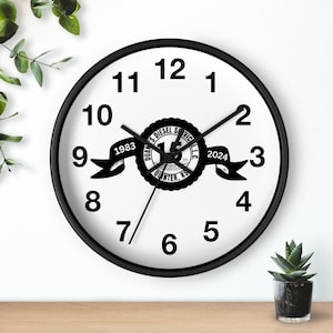 May include: Black and white wall clock with black hands. The clock face has black numbers and a black and white logo that says "Quan's Diesel Service LLC 15th Anniversary 1983-2024 Quinter, KS".