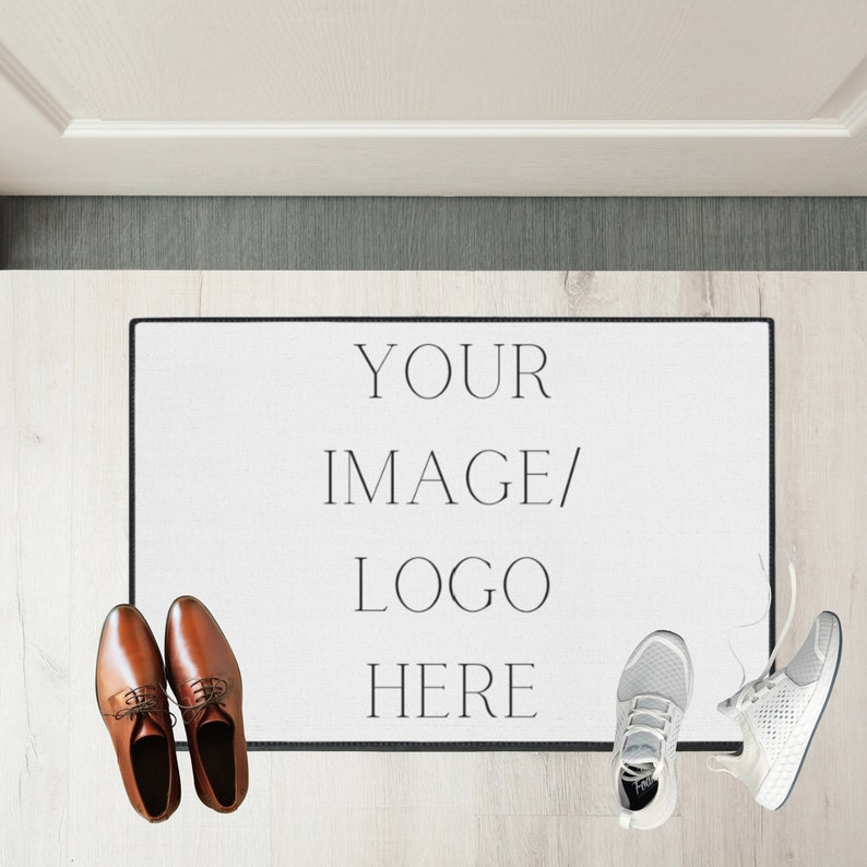 May include: White doormat with black border and text "YOUR IMAGE/LOGO HERE" on a light wood floor. Two pairs of shoes are on the floor, one pair is brown leather and the other is white athletic shoes.