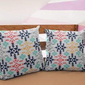 May include: Two decorative throw pillows with a geometric pattern in shades of blue, red, green, yellow, and gray. The pillows are on a wooden bed frame with a pink and white striped wall behind them.