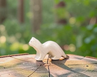 May include: A small, hand-carved wooden figurine of a ferret or weasel. The sculpture features a smooth, light-colored wood grain finish with a darker, textured tail tip. The animal is depicted in a standing, alert posture with a pointed snout.