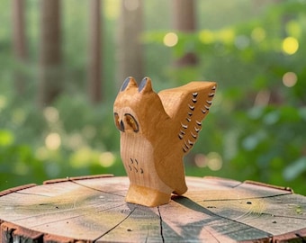 May include: A hand-carved wooden owl figurine featuring a light brown natural wood grain finish. The owl has painted black details on its wings, chest, and around its yellow eyes, with pointed ear tufts and wings extended in a stationary pose.