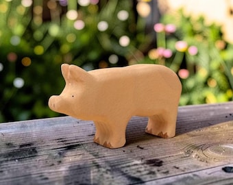 May include: A light tan wooden pig figurine with a smooth, matte finish. The animal figure features carved ears, a snout with two small dots for nostrils, and four sturdy legs. The surface of the wood shows a natural grain pattern throughout.