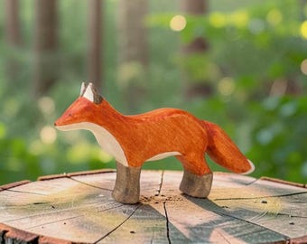 May include: A hand-carved wooden fox figurine featuring a vibrant orange coat, a white underbelly, and dark brown legs. The fox is depicted in a standing position with its head turned slightly to the side, showcasing smooth, rounded edges and wood grain.