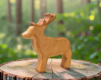May include: A hand-carved wooden figurine of a deer standing in profile. The object features a smooth, light brown natural wood grain finish with visible texture. The deer has a rounded head, a short snout, and stylized antlers extending upward.