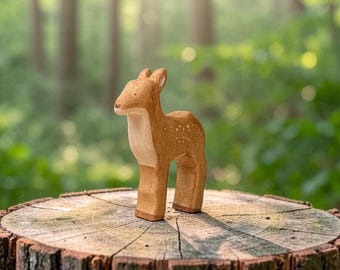 May include: A light brown wooden figurine of a standing fawn. The animal figure features a smooth, carved surface with visible wood grain, small painted white spots along its back, and dark brown painted hooves, captured in a side profile view.