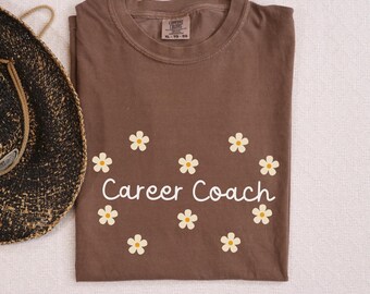 May include: Brown t-shirt with white daisy flowers and the text "Career Coach" printed on the front.