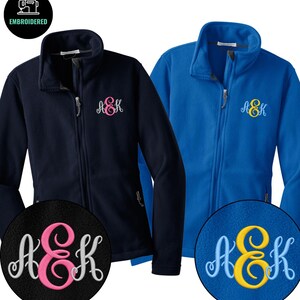 May include: Two fleece jackets with full-length zippers and stand-up collars. One jacket is navy blue with pink and white embroidered monogram letters AEK. The other jacket is royal blue with yellow and light blue embroidered monogram letters AEK.
