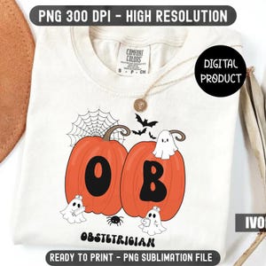 May include: Ivory-colored t-shirt featuring a Halloween-themed design. Two orange pumpkins with the letters "O" and "B" are displayed, along with a spider web, bats, and ghosts. The text "OBSTETRICIAN" is printed below the pumpkins. The shirt is a digital product.