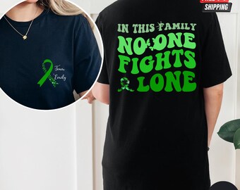 May include: Black t-shirt with green text that reads "In this family no one fights alone". The back of the shirt features a green ribbon with the text "Team Emily".