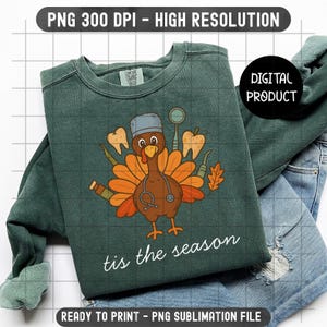 May include: A dark green sweatshirt with a turkey graphic wearing a dentist's hat and stethoscope, surrounded by teeth and dental tools. The text "tis the season" is written in white script. The sweatshirt is paired with blue jeans.