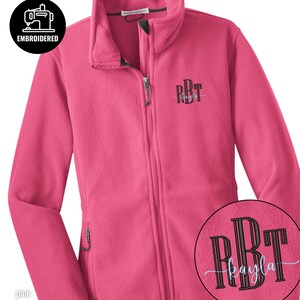 May include: A pink fleece jacket with a full zipper and a high collar. The jacket has the embroidered initials "RBT" on the chest. A circular patch shows the initials "RBT" and the name "kayla". The jacket has the word "embroidered" and "pink blossom" on it.