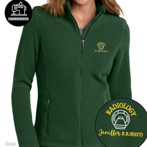 May include: Forest green fleece jacket with a full zipper and two side pockets. The jacket has an embroidered logo that says "RADIOLOGY" and the name "Jeniffer R.R.(CT)". The jacket also has a small embroidered logo that says "EMBROIDERED".