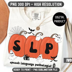 May include: Ivory-colored t-shirt with a Halloween-themed design. Features three orange pumpkins with the letters "SLP" and ghost illustrations. The text "Speech Language pathologist" is below the pumpkins. Includes bats and a spiderweb.