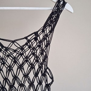 Peut inclure: Top en crochet noir avec un motif délicat et complexe. Le haut est suspendu à un cintre blanc.