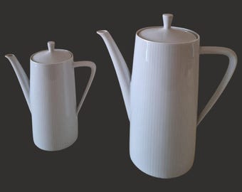 May include: Two white ceramic coffee pots with lids and handles. The larger pot is taller than the smaller pot.