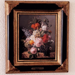 Puede incluir: Pintura enmarcada de naturaleza muerta floral. La obra presenta una cesta rebosante de flores coloridas, incluyendo rosas, tulipanes y otras flores. El marco es negro con detalles dorados.