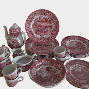 Può includere: Un servizio da tè vintage con un motivo transferware rosso e bianco. Il set include una teiera, tazze, piattini, piatti, una lattiera e una zuccheriera. I piatti e le ciotole presentano un design paesaggistico dettagliato.