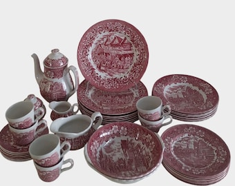 May include: A vintage tea set with a red and white transferware pattern. The set includes a teapot, cups, saucers, plates, a creamer, and a sugar bowl. The plates and bowls have a detailed landscape design.
