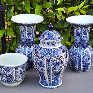 May include: Four blue and white ceramic vases with intricate floral designs. The vases are arranged on a grey surface. Two of the vases are tall and slender, while the other two are shorter and wider.