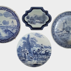May include: Four blue and white decorative plates with Dutch landscape scenes. The plates are round and oval, featuring windmills, canals, and figures. The plates are made of ceramic and are displayed against a white background.