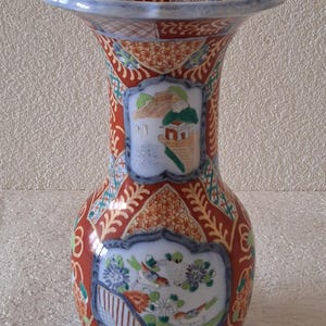 Könnte beinhalten: Eine dekorative Keramikvase mit ausgestelltem Rand und bauchigem Körper. Die Vase hat einen roten Hintergrund mit komplizierten Mustern und detaillierten gemalten Szenen von Landschaften und Vögeln. Der Rand und der Boden sind blau, und die Vase hat eine glänzende Oberfläche.