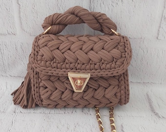 May include: A brown crocheted handbag with a gold chain strap and a gold clasp. The bag has a braided handle and a tassel.